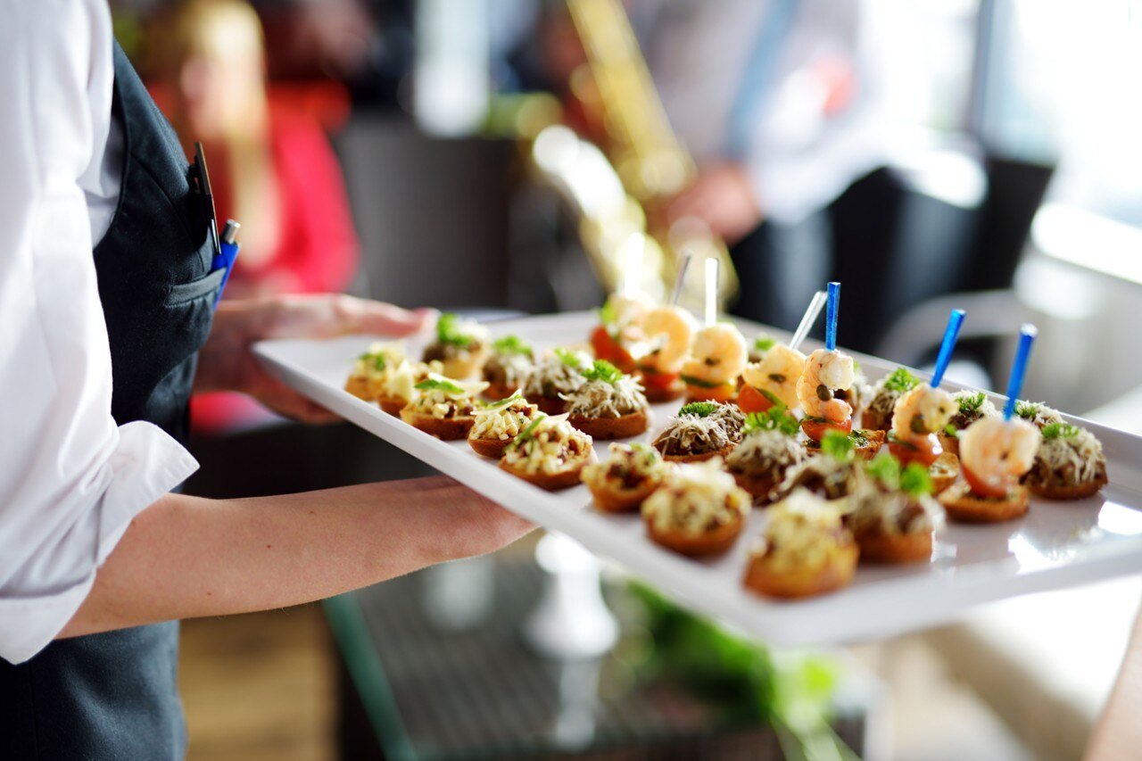 Person holding a tray of assorted canapés or appetizers at a social event.