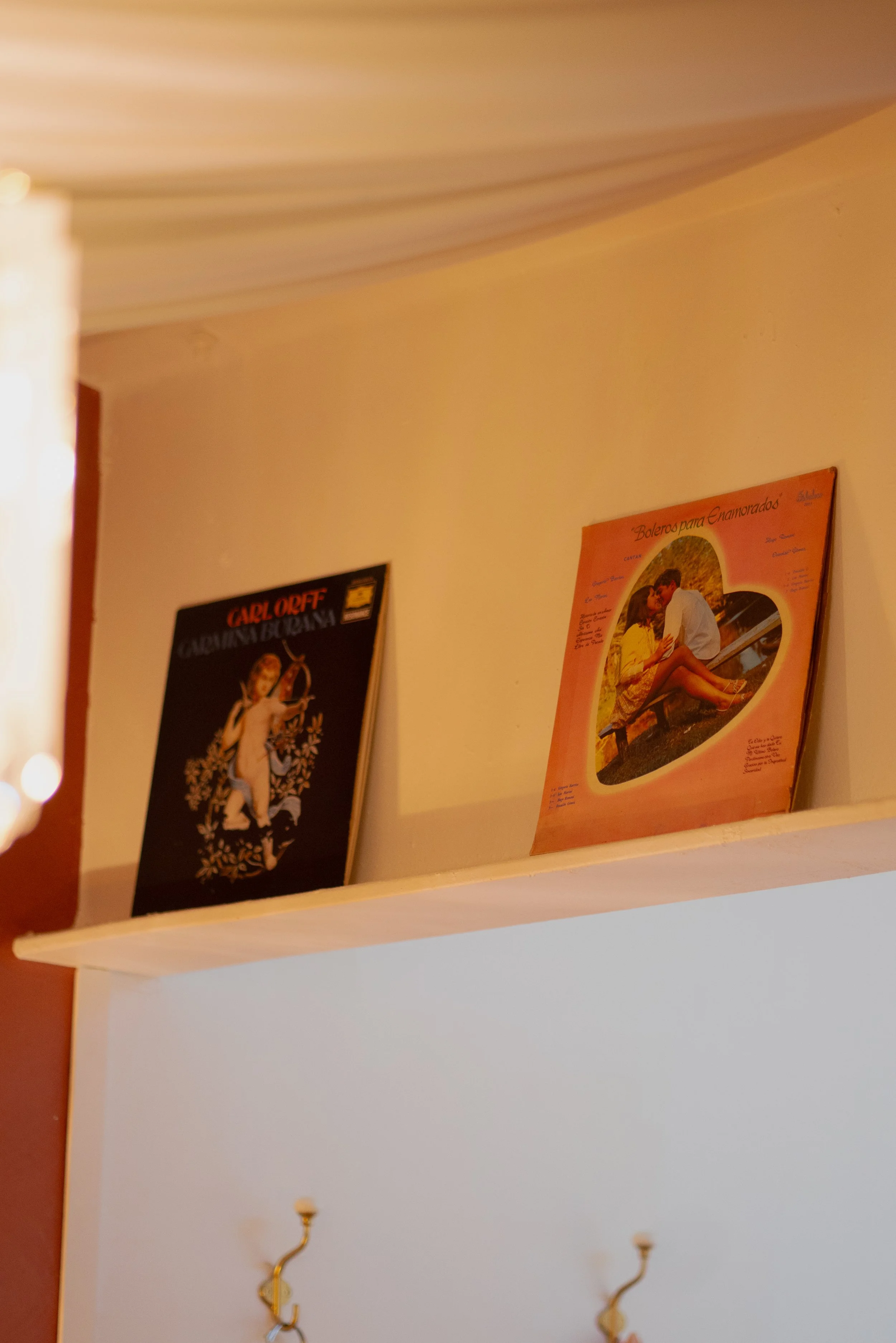 Close-up of a wall shelf with two vintage posters, one black and red, the other pink with a romantic scene, and some hooks below.
