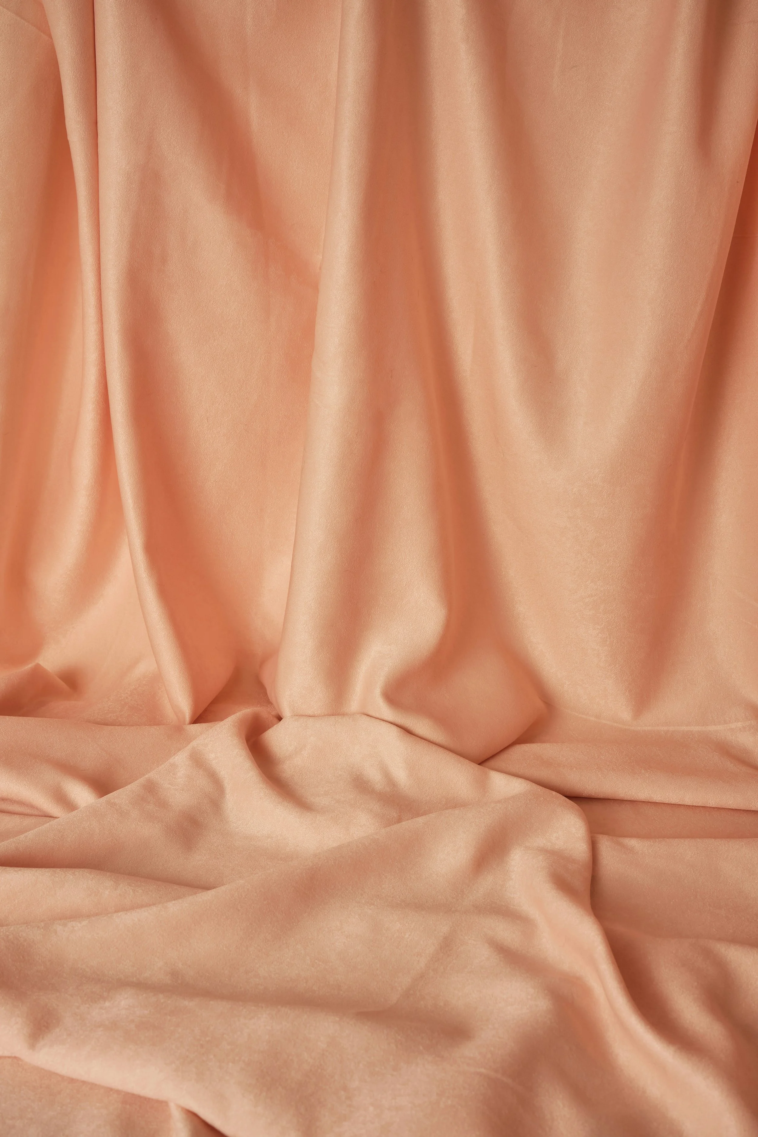 Peach-colored satin fabric draped and gathered, creating soft folds and a smooth, shiny surface.