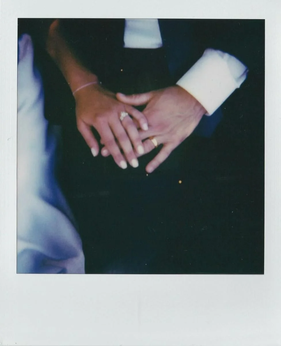 Close-up of a bride and groom holding hands during a wedding ceremony, showing wedding rings, with the bride's hand on top of the groom's.