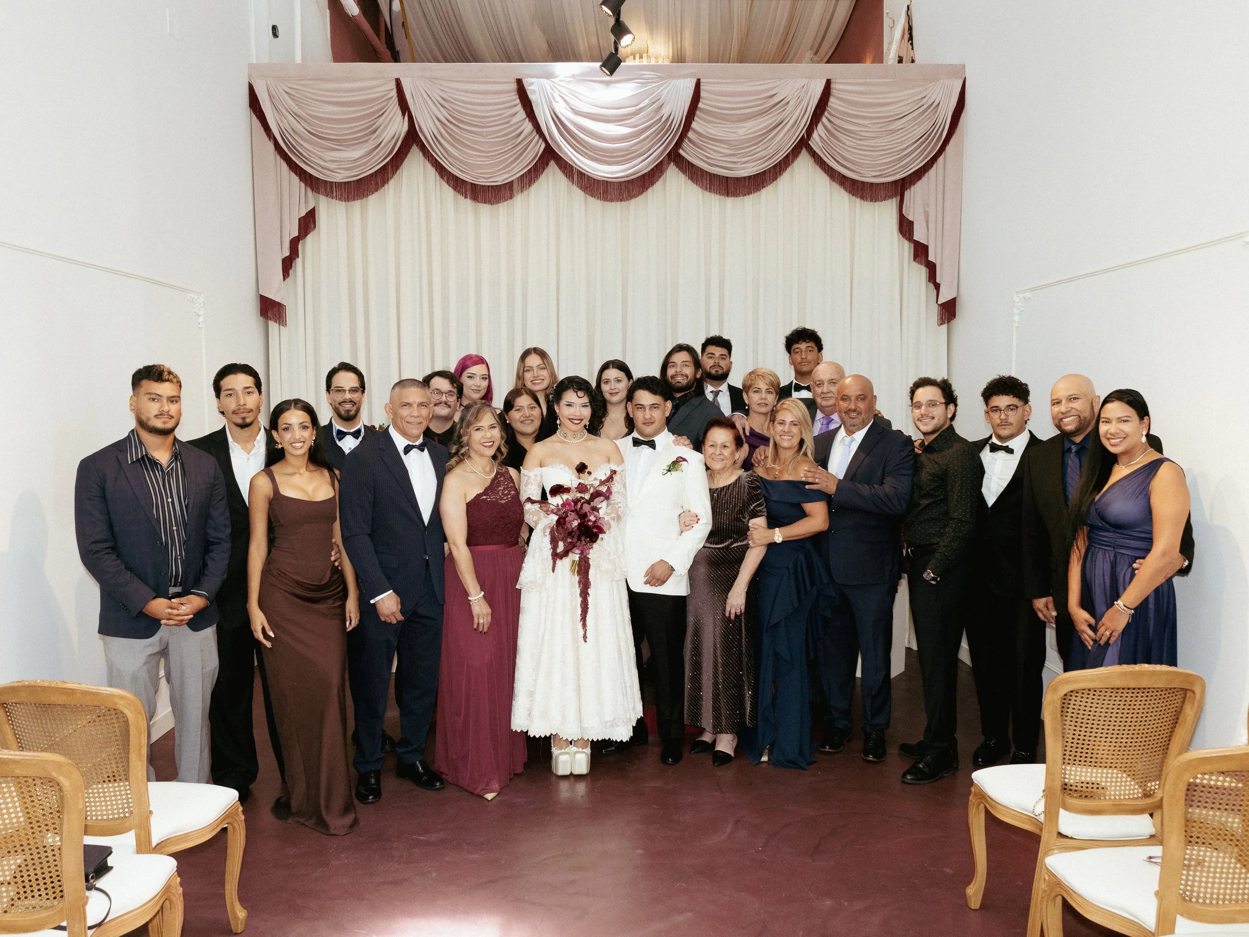 A family dressed in formal attire, gathered together at the altar with a draped curtain backdrop, celebrating a wedding