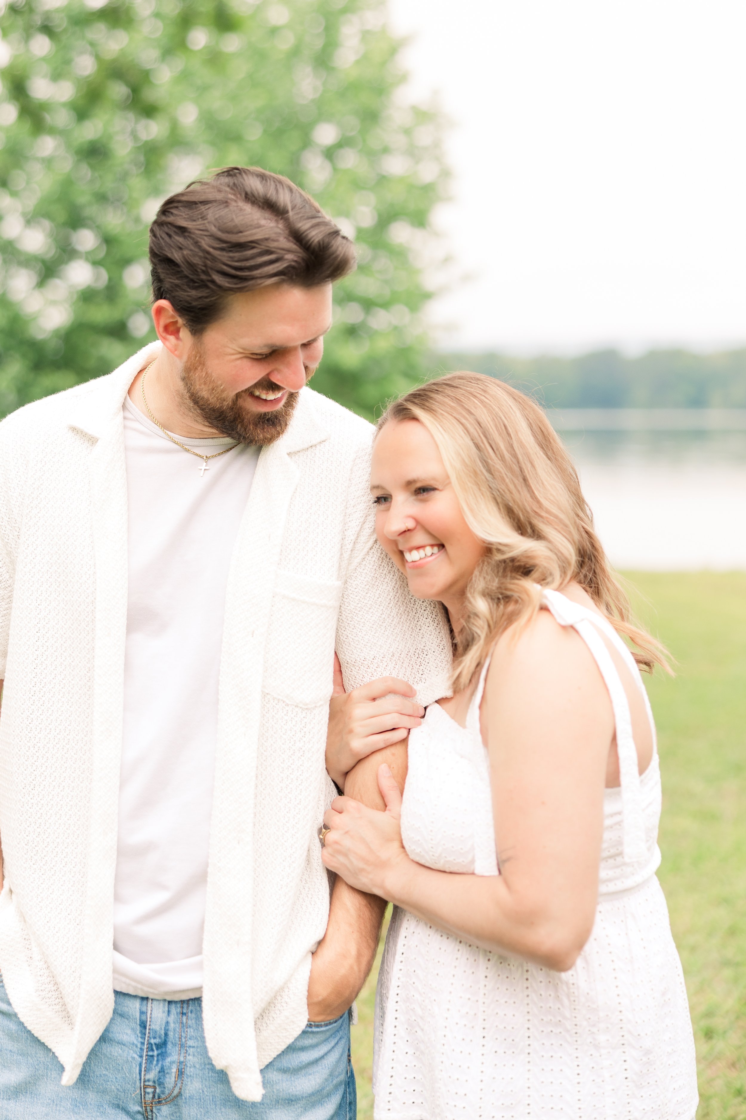 A young couple smiling and embracing outdoors near a lake on a cloudy day.