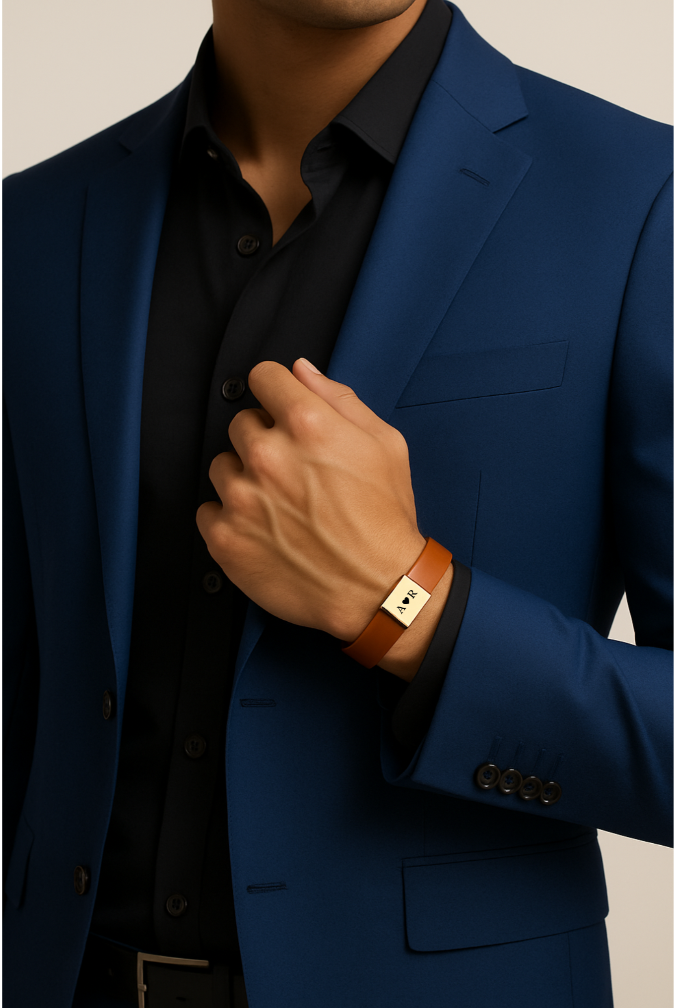 Close-up of a man wearing a blue suit and black shirt, showing a brown leather bracelet with gold plate engraved with initials 'A R' on his wrist.