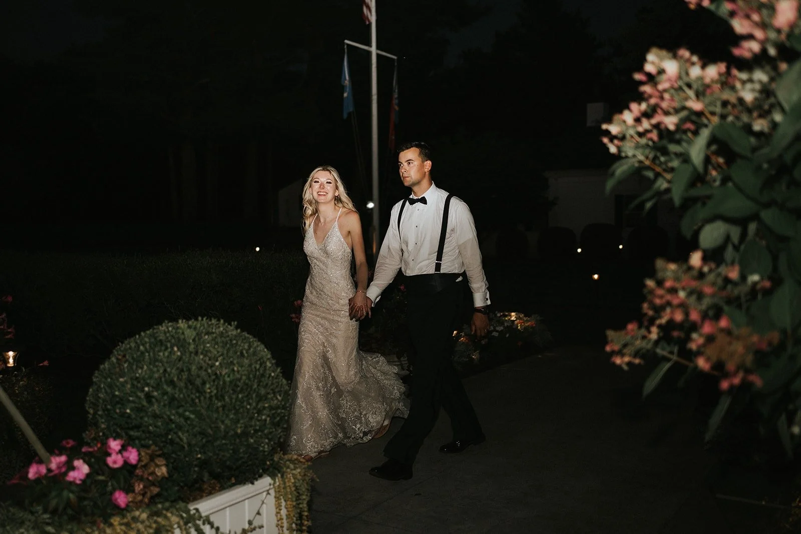 A bride and groom walking hand in hand outdoors at night during their wedding celebration.