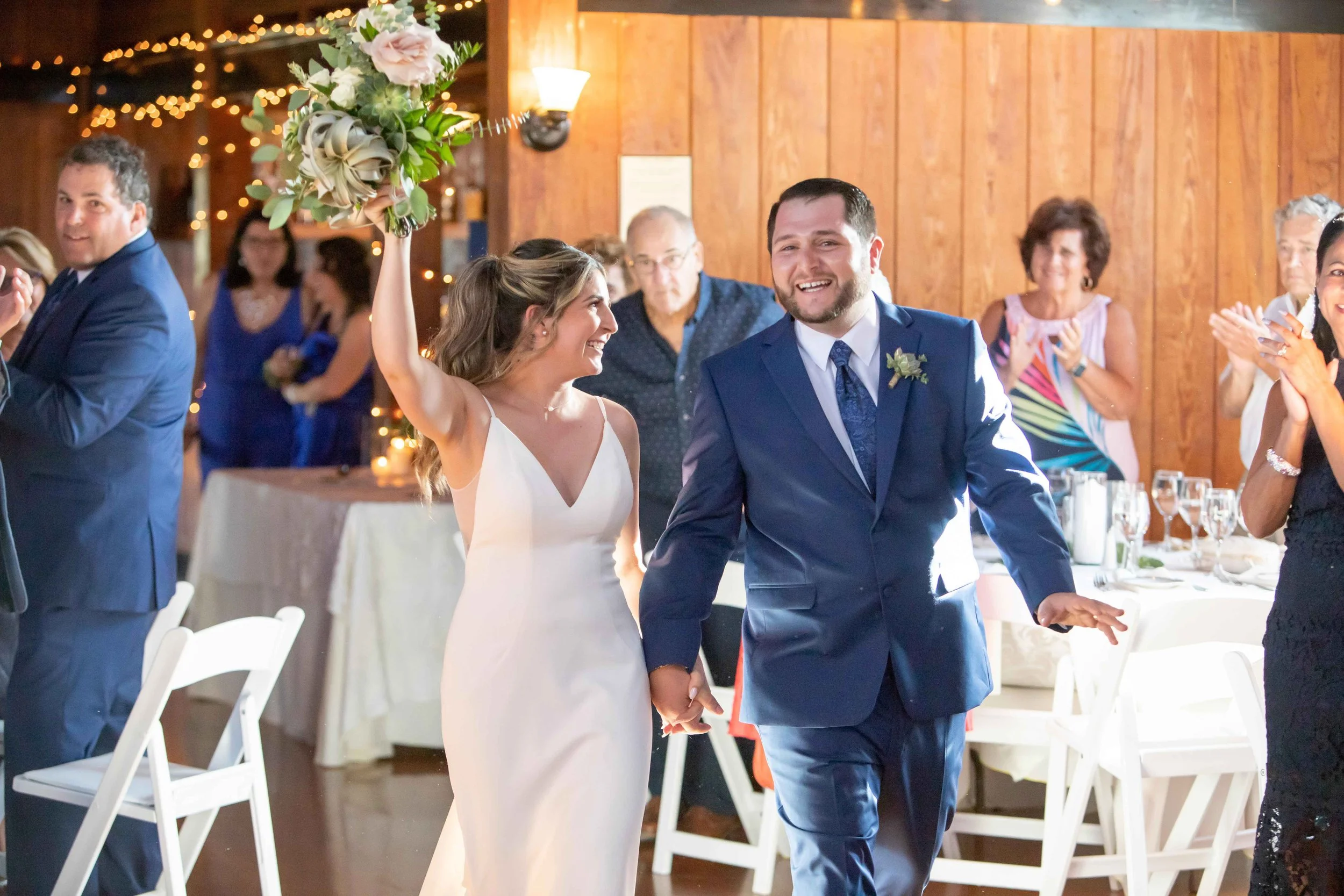A bride and groom walking hand in hand at their wedding reception, surrounded by guests who are clapping and celebrating.