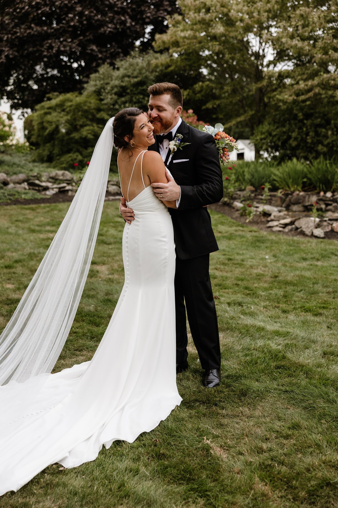 A bride and groom embrace outdoors during their wedding, smiling and happy.
