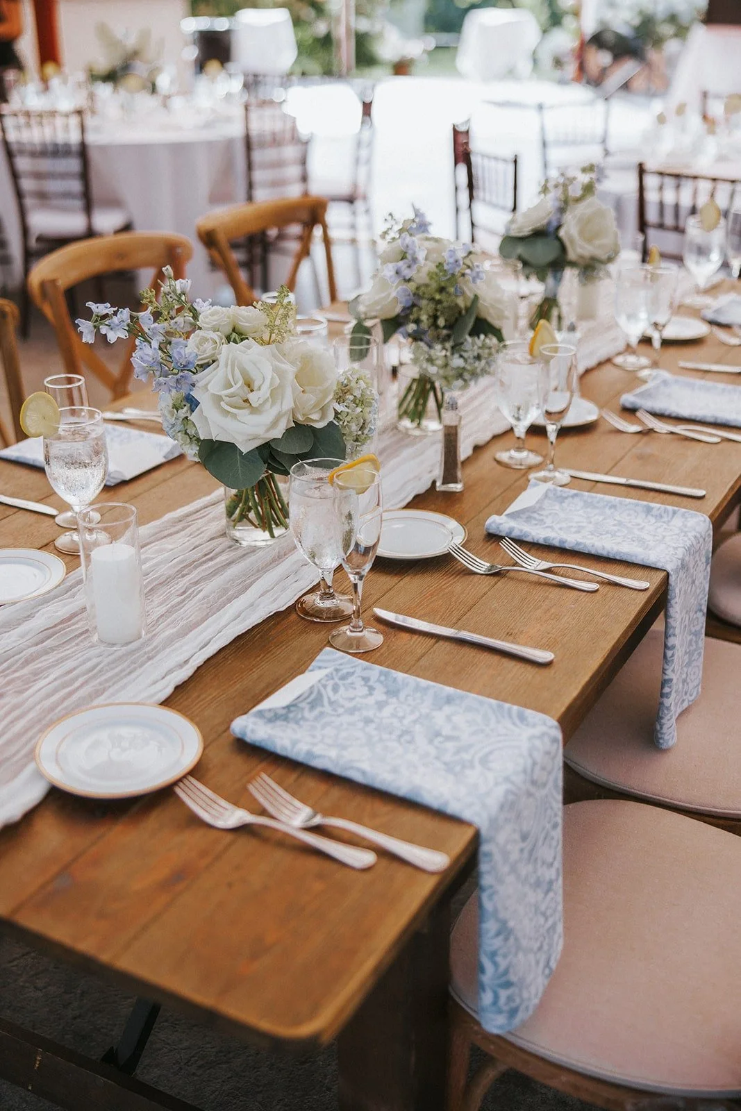 A softly lit dining table set for a formal event with white floral centerpieces, water glasses with lemon slices, plates, and silverware arranged neatly with light blue patterned napkins.