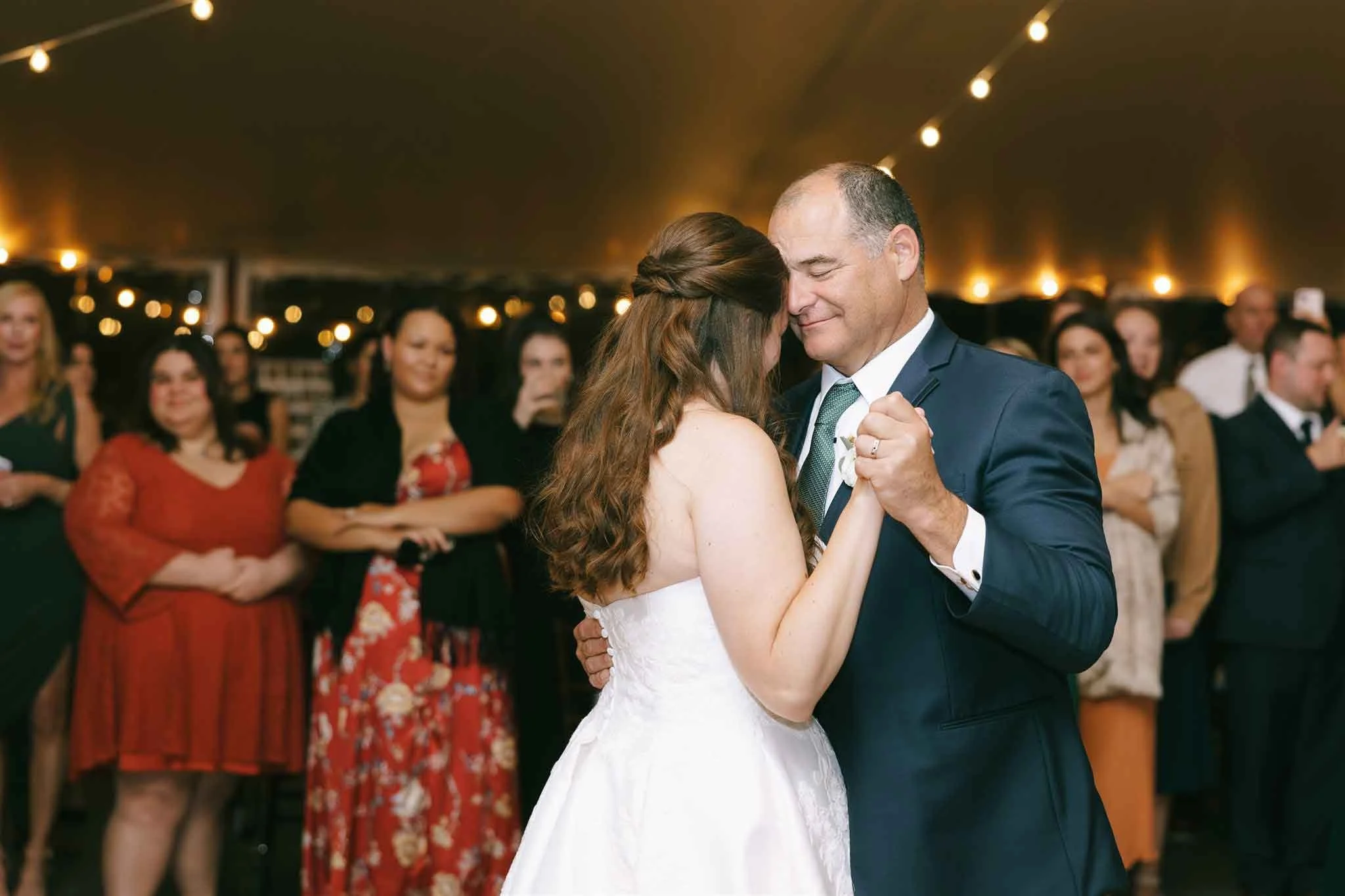 A bride and groom share a dance at their wedding reception, surrounded by guests watching and smiling.