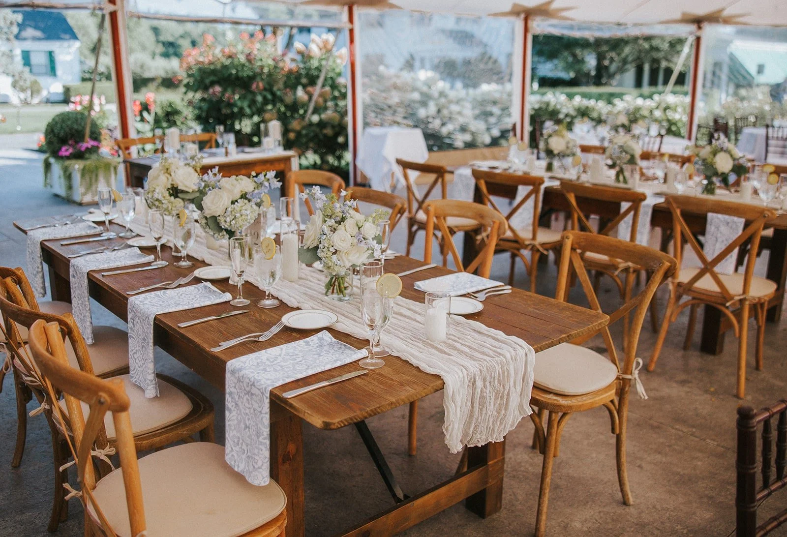 Wedding reception tables decorated with white flowers, candles, and elegant place settings in a tented outdoor space with pink and green floral arrangements.