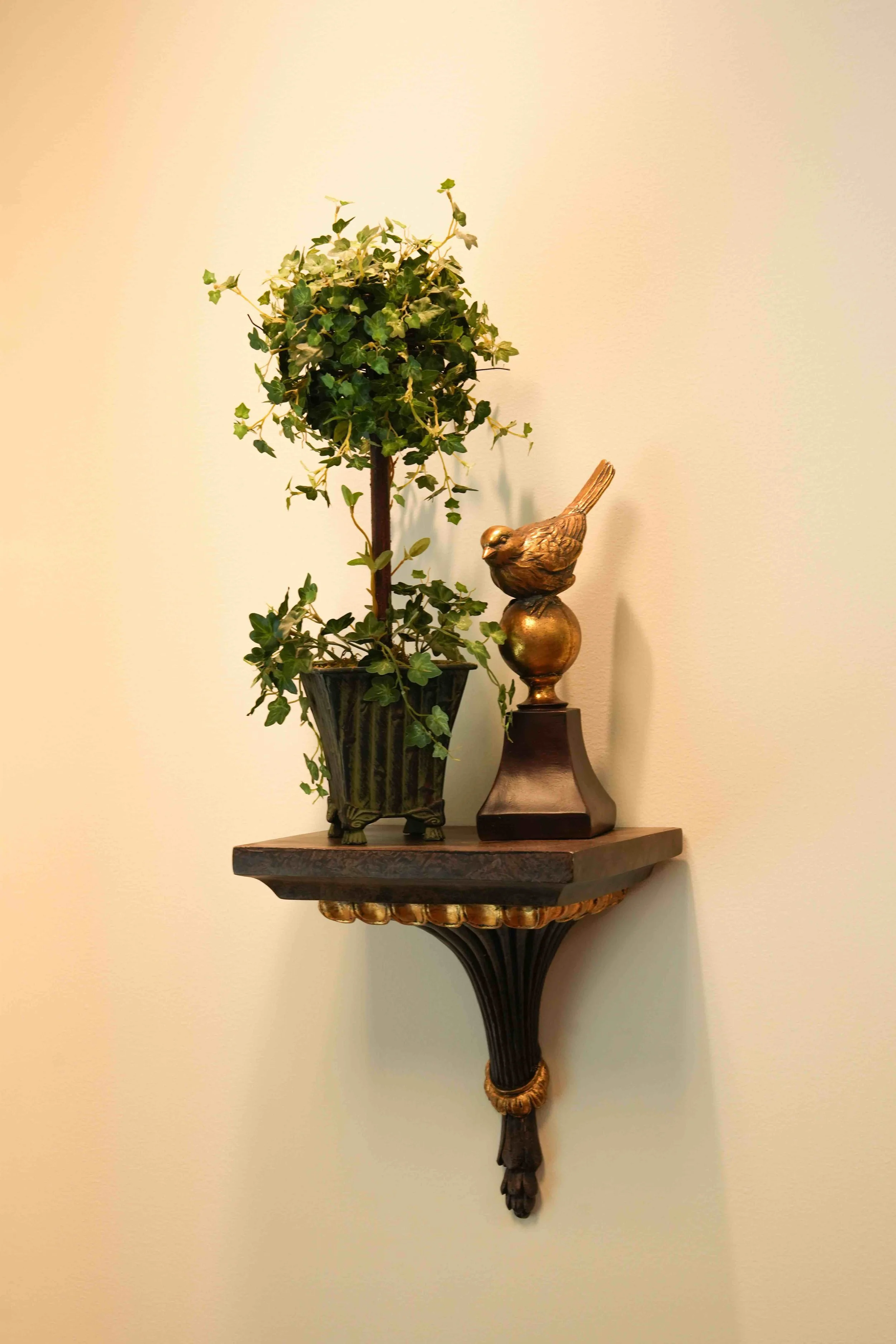 Decorative wall shelf with a potted ivy plant and a gold-colored bird figurine on a stand.