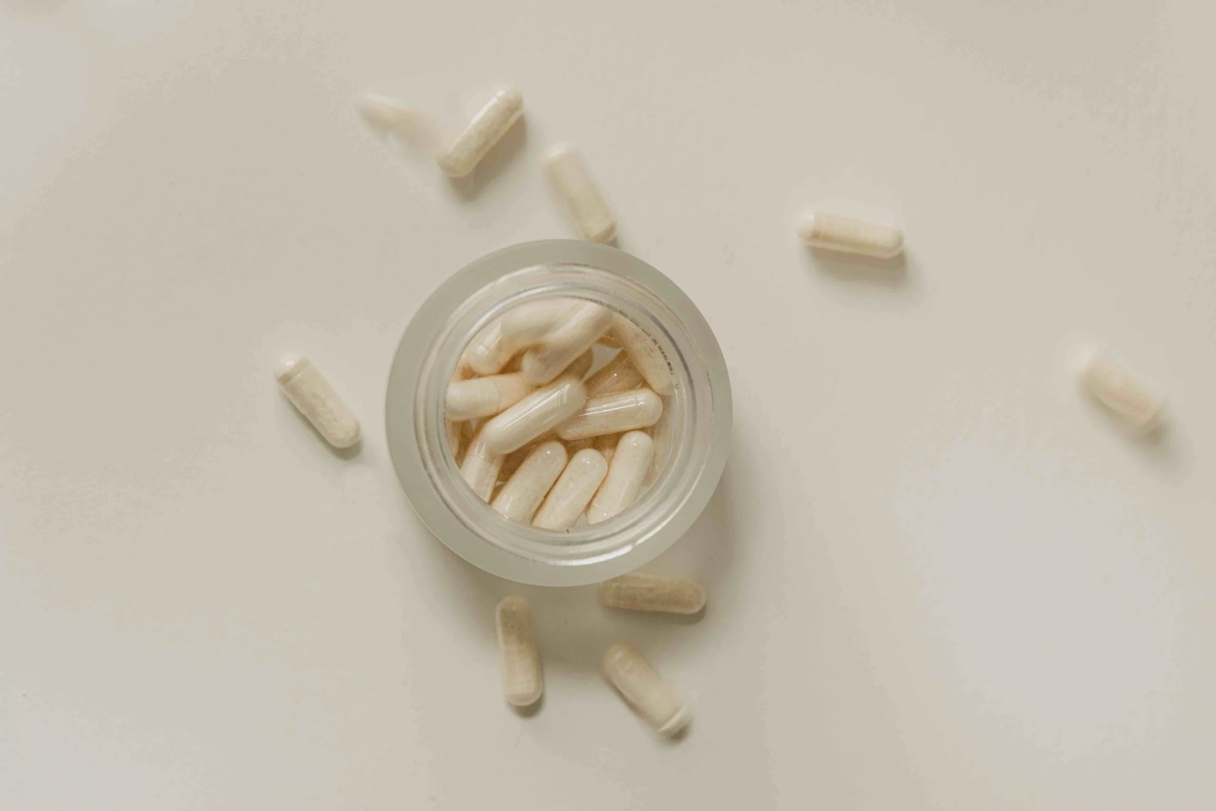 A white bottle filled with capsules, some capsules spilled around on a white surface.