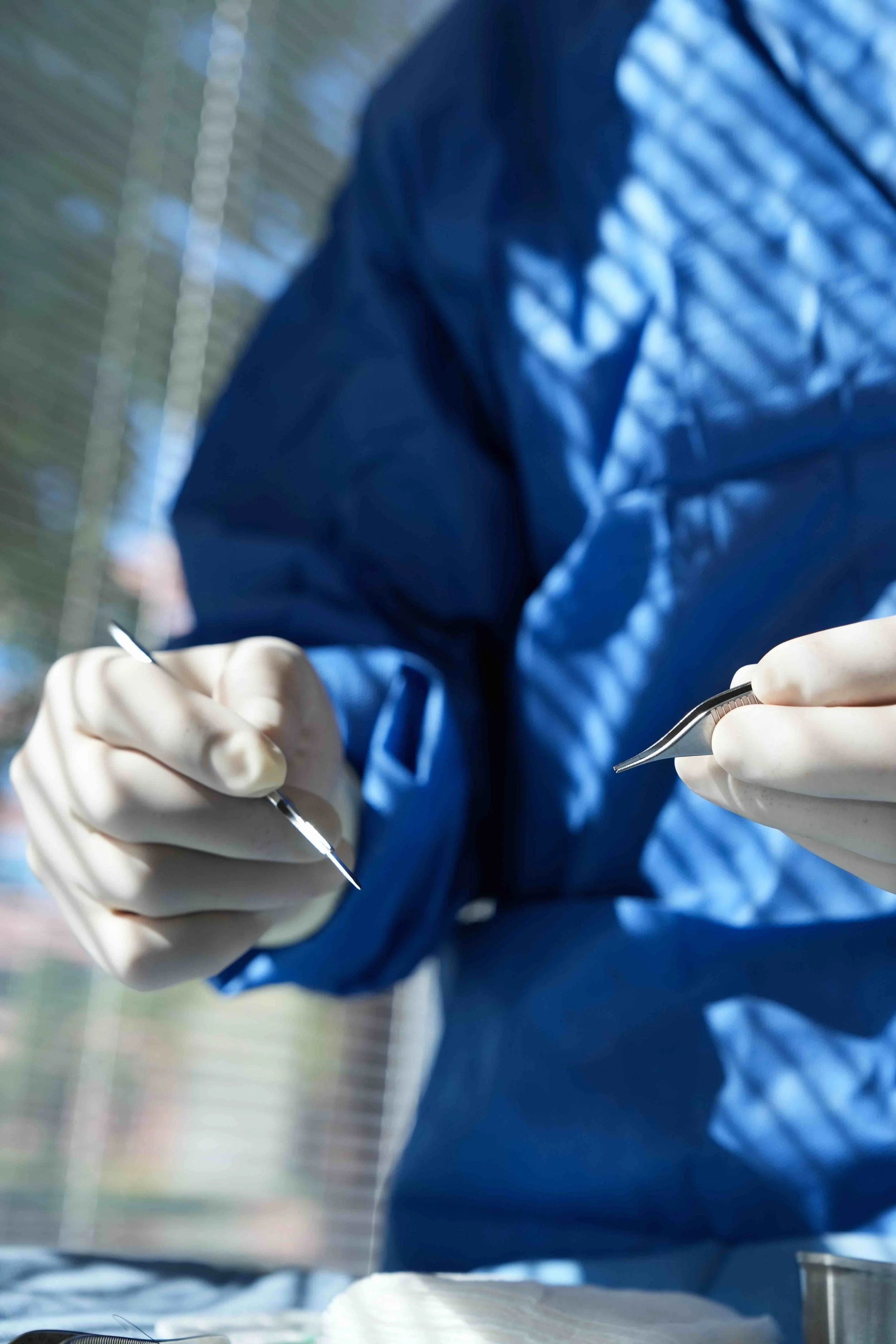 Close-up of a surgeon wearing gloves and a blue protective suit, holding surgical tools during a procedure.