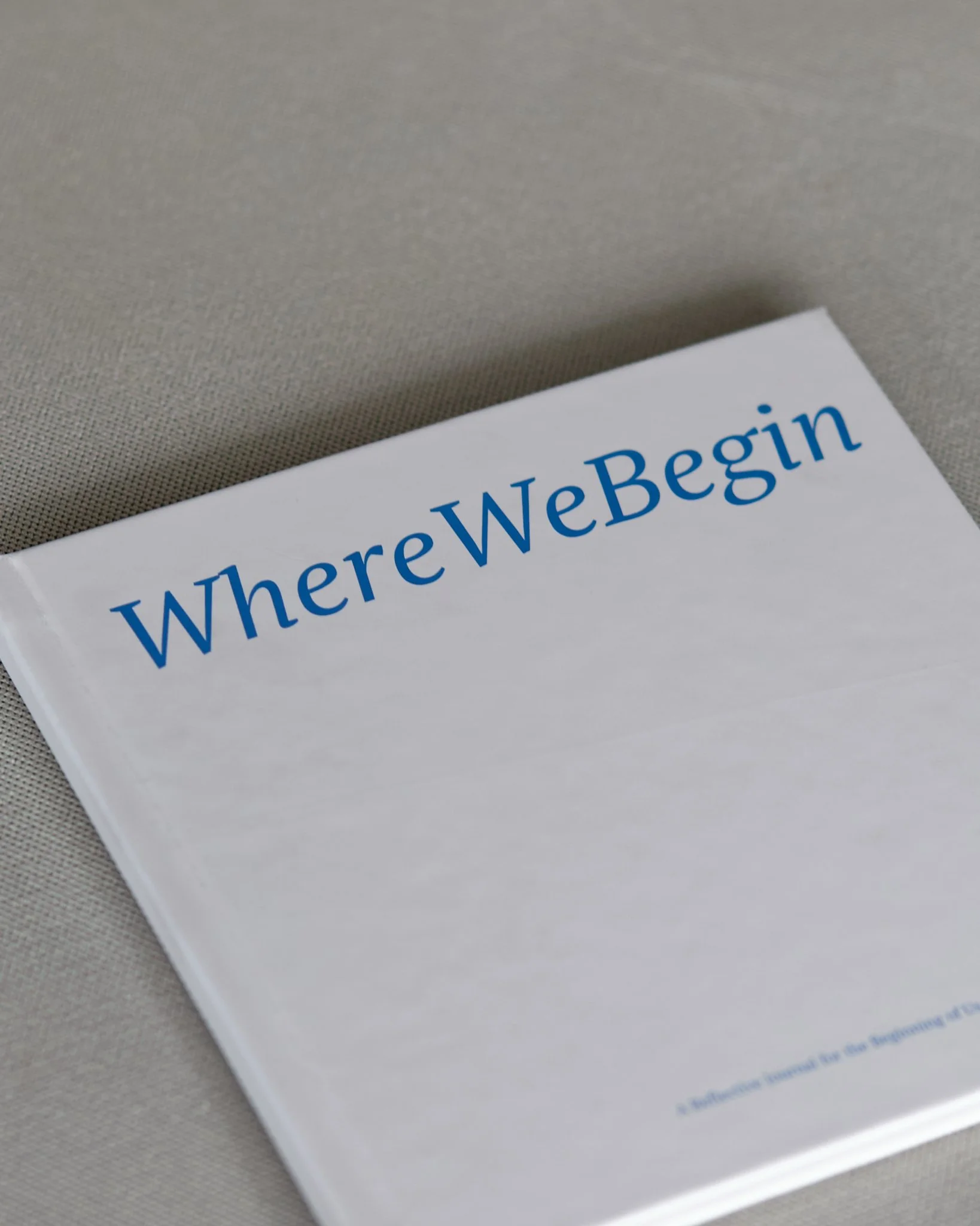 A booklet titled 'WhereWeBegin' resting on a light-colored fabric surface.