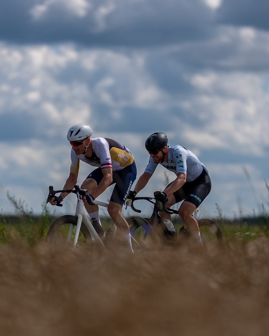 Two road cyclists racing side by side across open countryside under a big cloudy sky