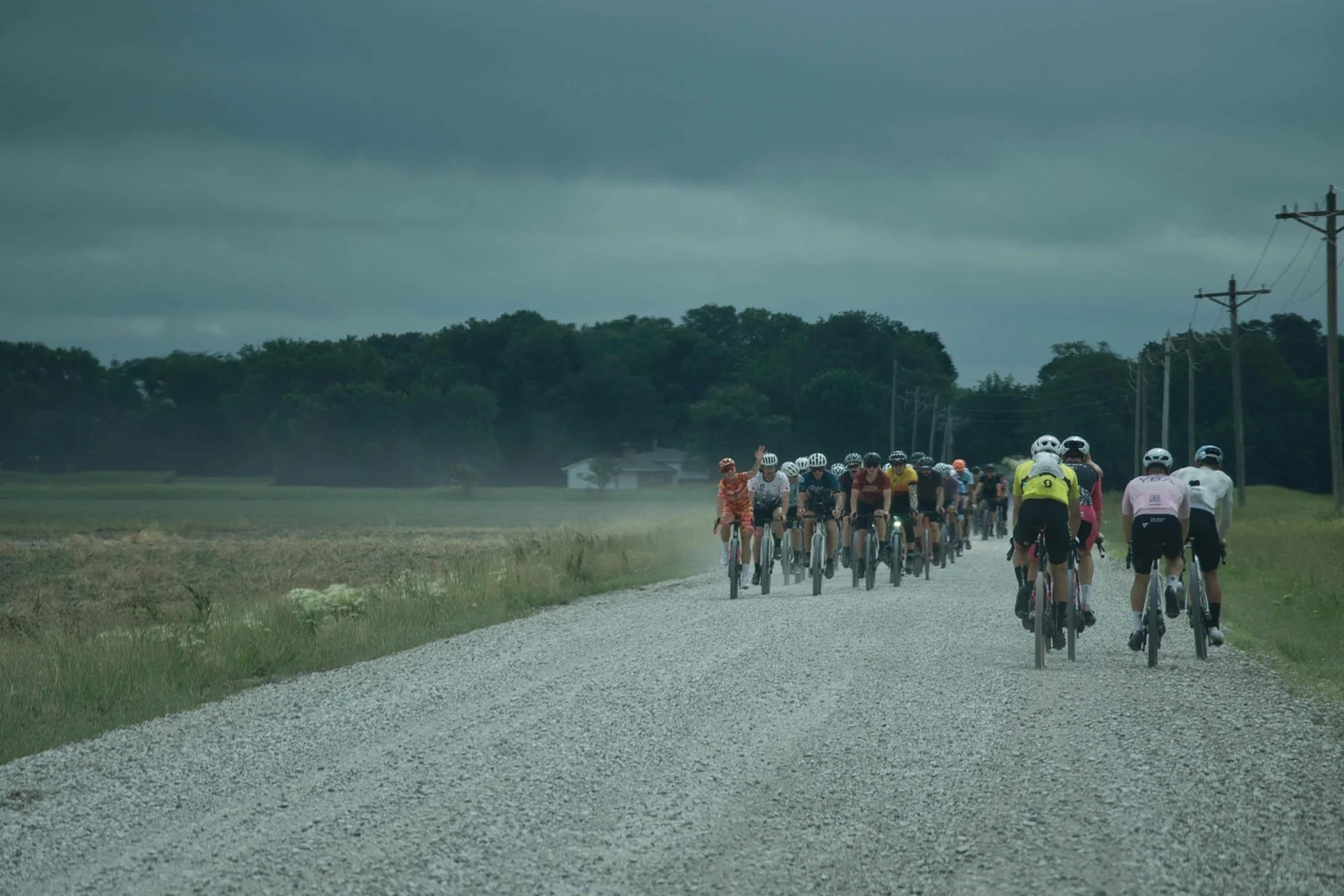 A long line of riders on a gravel road under a dark storm sky, USA