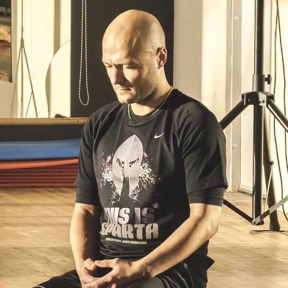 Jānis Mūsiņš uz vingrošanas paklājiņa zālē, T-kreklā ar uzrakstu This is Sparta