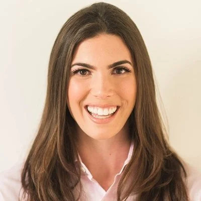 Portrait of a young woman with long brown hair, smiling with straight teeth, wearing a light pink shirt.
