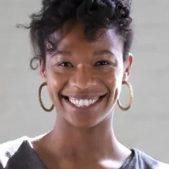 Close-up of a smiling Black woman with short curly hair, wearing hoop earrings, against a light background.