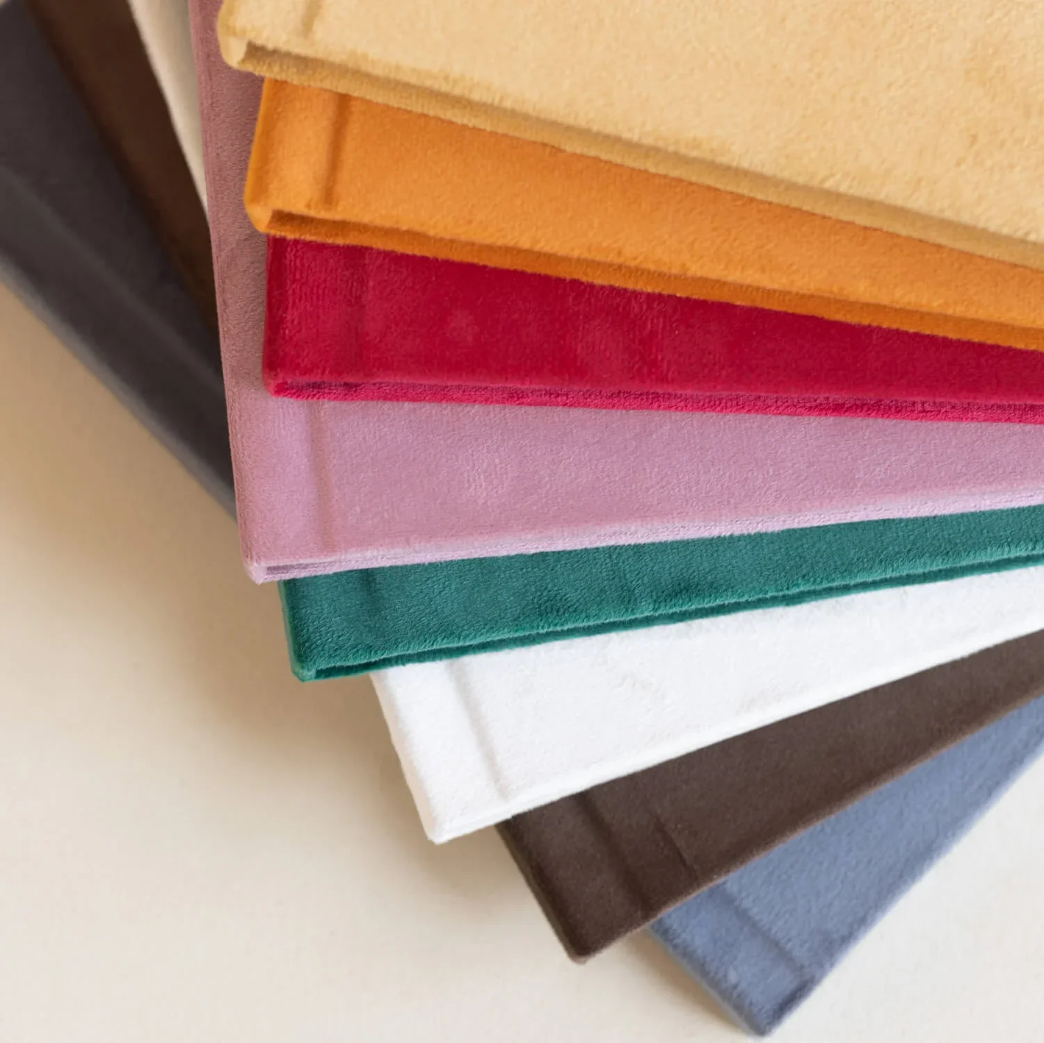 Stack of fabric swatches in beige, orange, red, pink, green, white, brown, and gray on a white surface.