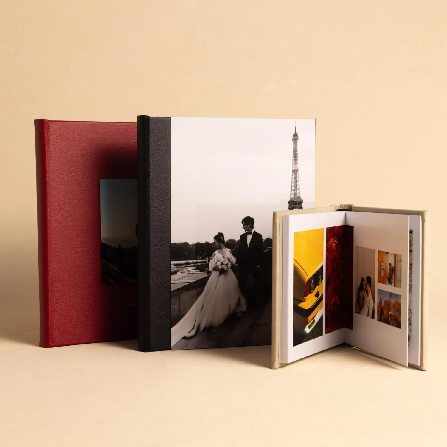 A set of three books, two closed and one open, with a background beige wall. The open book shows colorful photographs, while one of the closed books has a black cover with a cover photo of a wedding couple, and the other has a red cover.