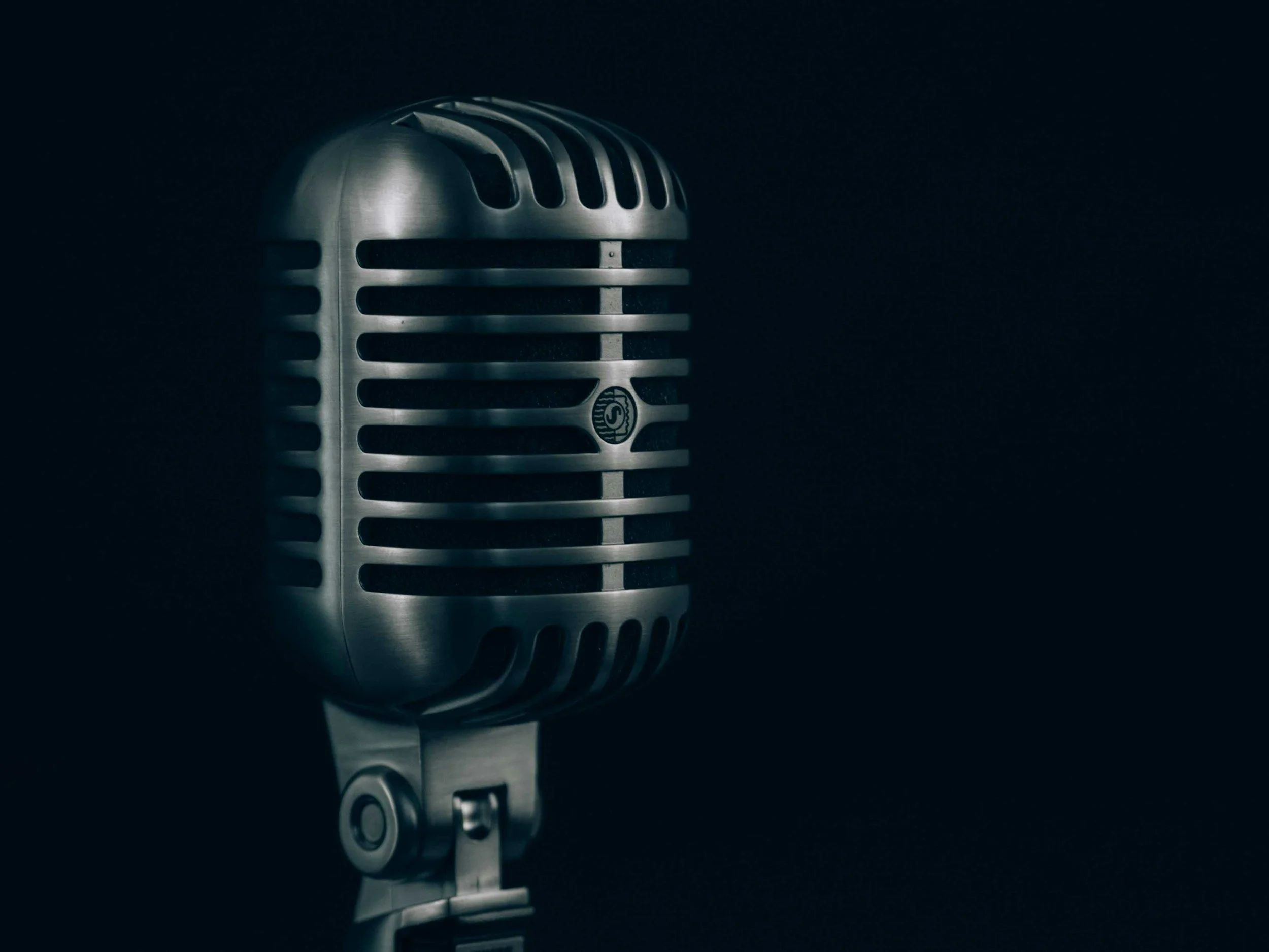 A vintage silver microphone on a stand against a dark background.