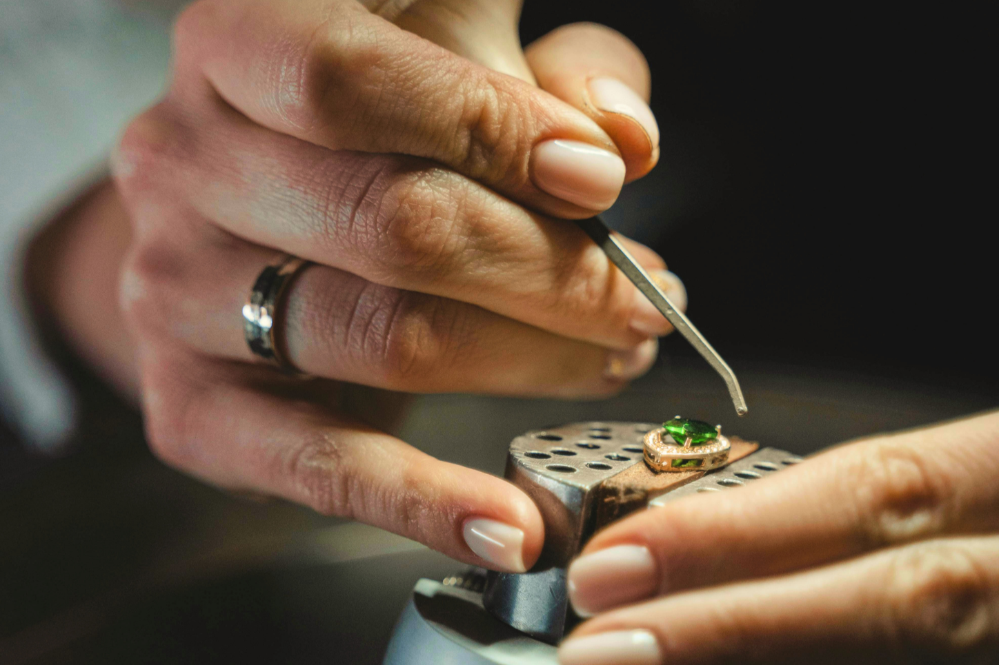 L'orfèvre travaille sur une bague ornée d'une pierre verte, en utilisant un outil précis, dans un atelier de bijouterie.