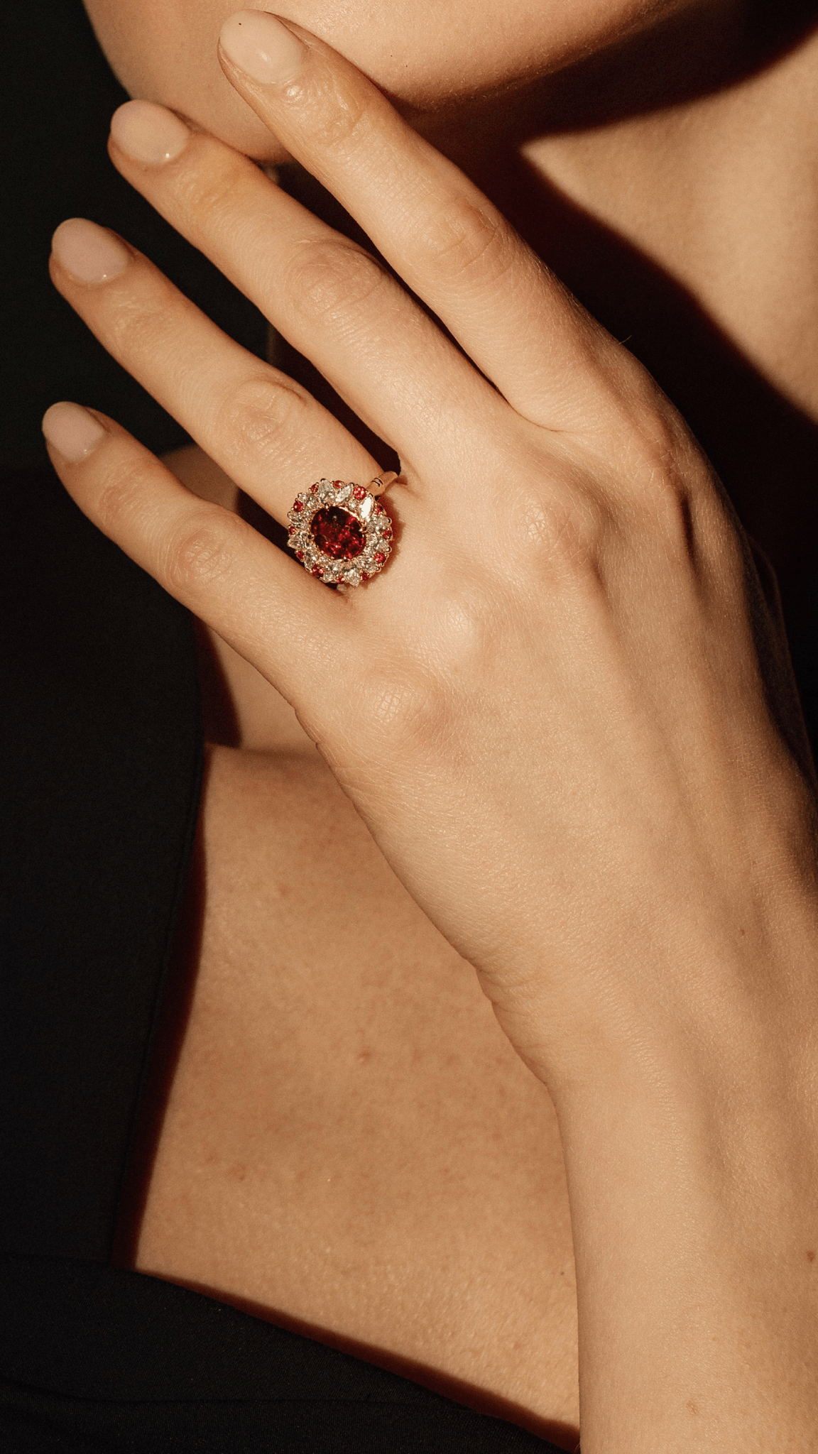 Une main portant une bague avec un gros rubis rouge entouré de diamants, posée contre la peau nue.
