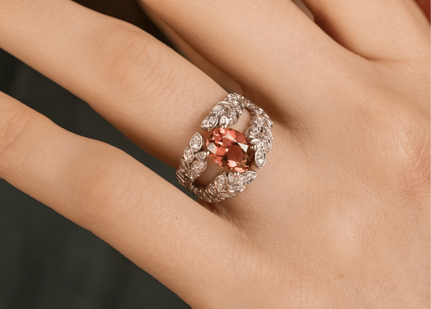 Bague en argent avec un gros pierre rose au centre entourée de petites pierres blanches, portée sur un doigt féminin.