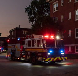 Fire truck with red and blue emergency lights activated on city street at night, near a brick apartment building.