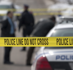 Blurred scene of police officers and a police car behind yellow police tape reading 'POLICE LINE DO NOT CROSS'.