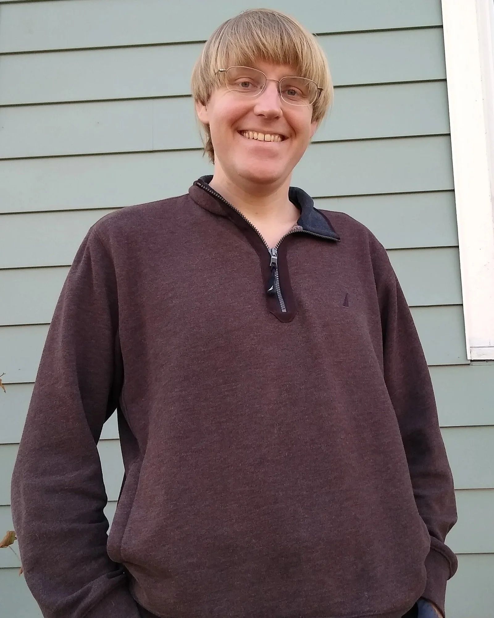 Max Brooke, a light skinned, blond man wearing a quarter zip sweater. The camera is at a slightly lower angle so he's smiling down at the camera.