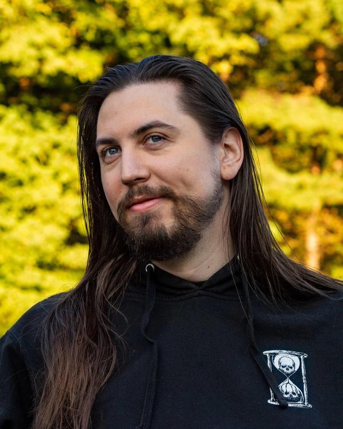 Dylan Grinder, he has light skin and long dark hair, wearing a black polo shirt and smiling at the camera.