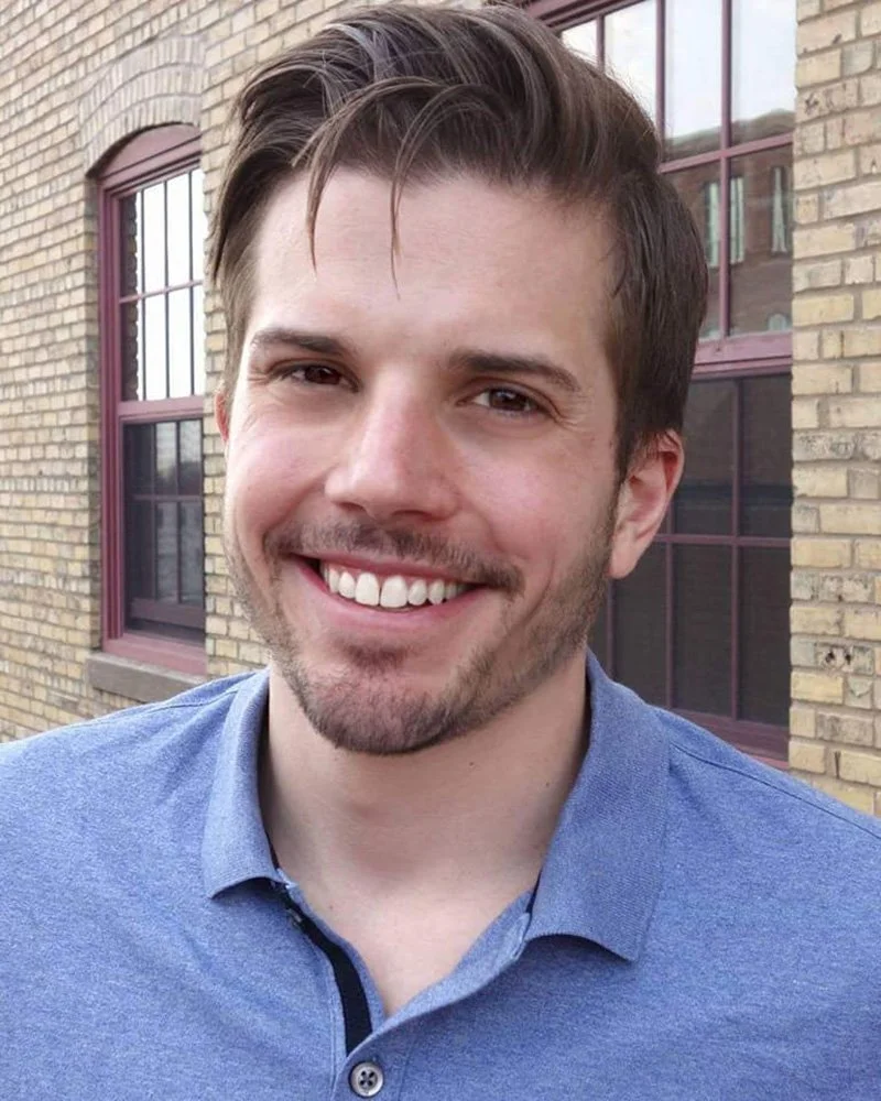Andrew Fischer, a light skinned man with short brunette hair, wearing a light blue polo shirt and smiling at the camera.