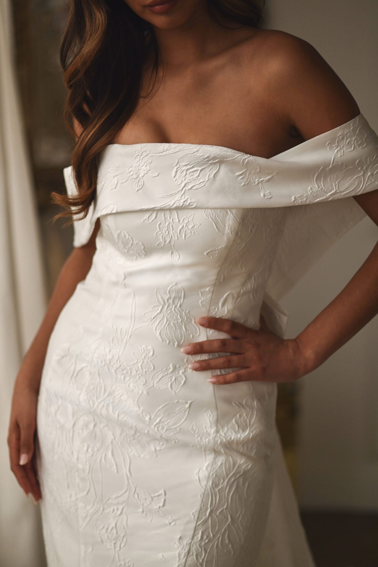 Close-up of a woman wearing an off-shoulder white dress with floral embroidery.