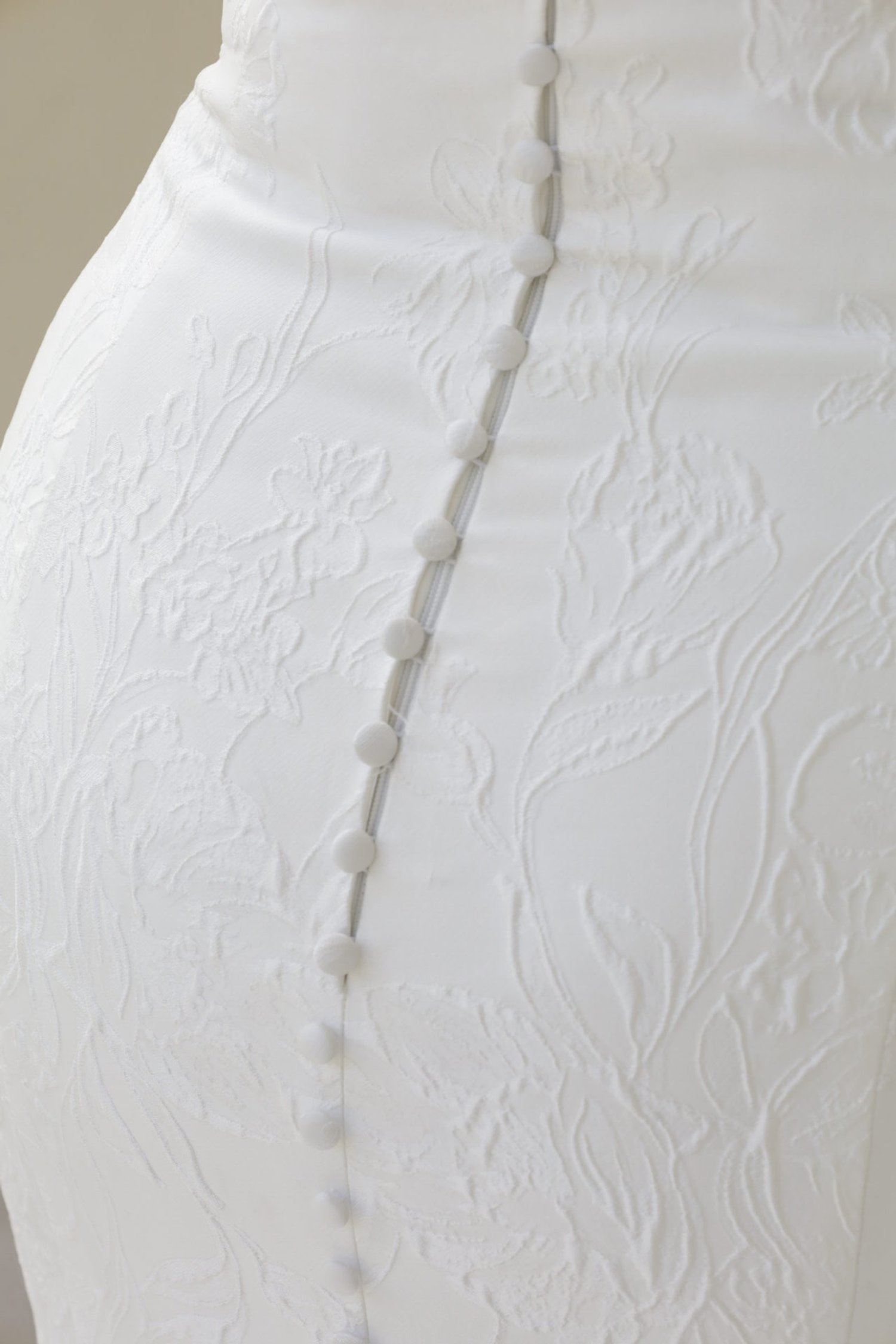 Close-up of a white wedding dress with textured floral embroidery and fabric-covered buttons down the back.
