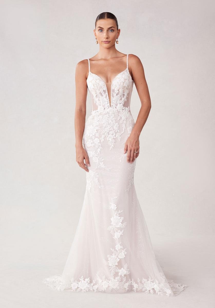 A woman in a fitted white wedding dress with floral lace details and a deep V neckline.
