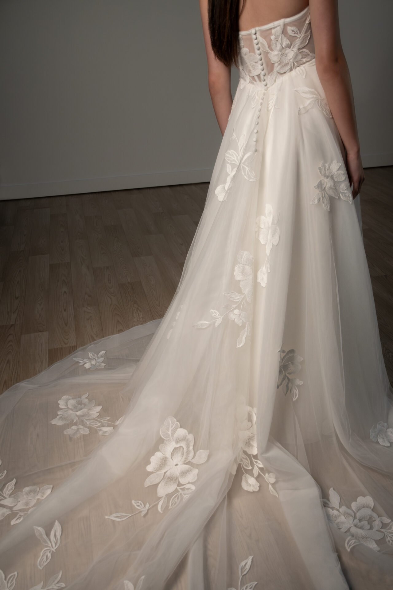 A woman wearing a white wedding dress with floral lace embroidery and a long train.