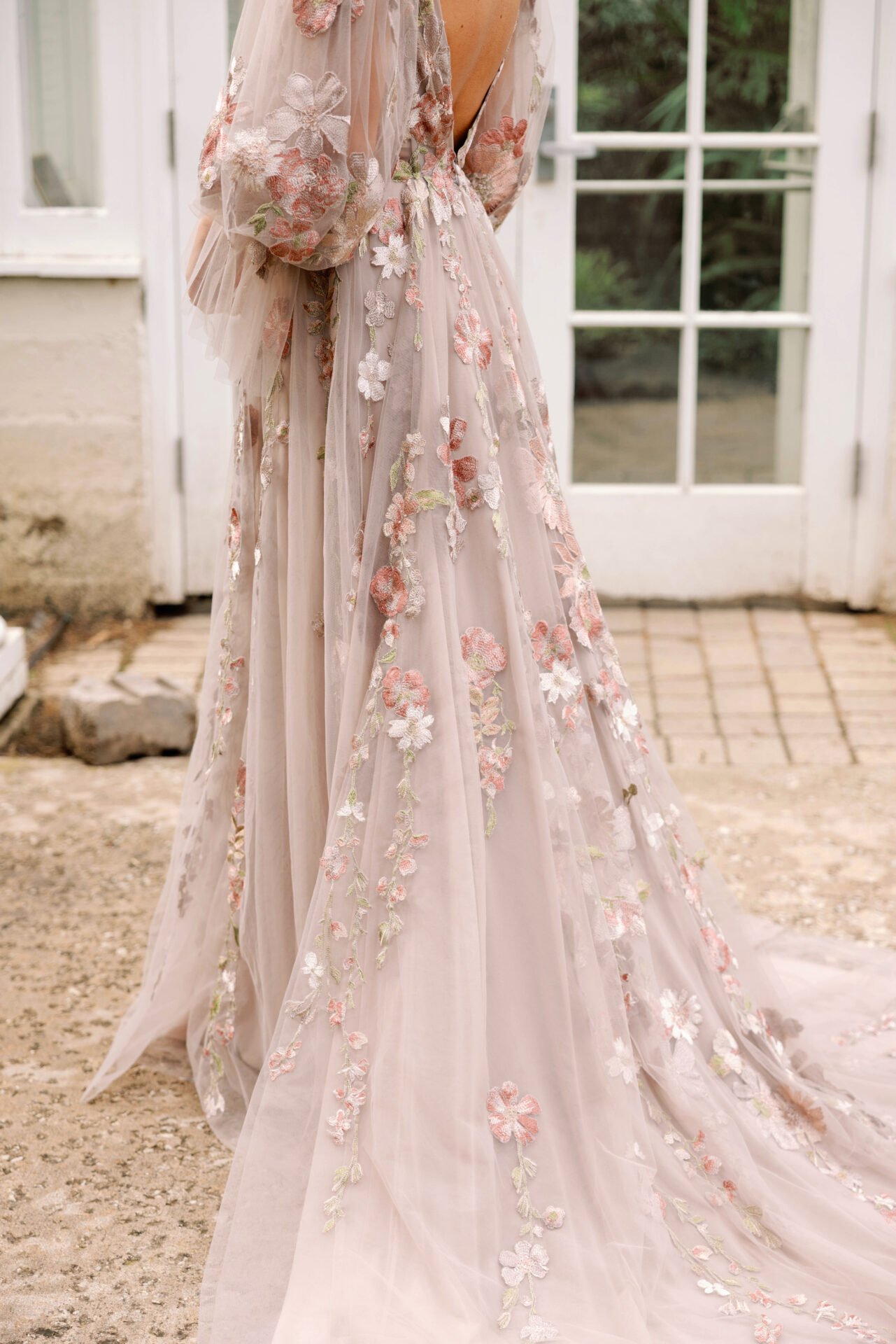 A long, flowing dress with pink, white, and green floral embroidery, hanging outside near a glass door.