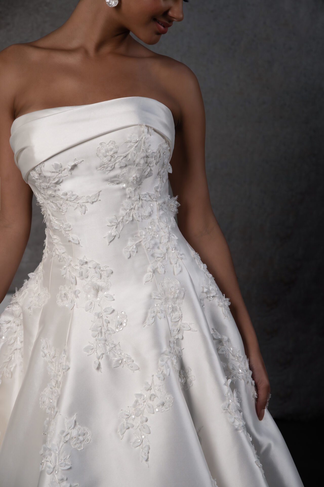 Close-up of a woman in a strapless white wedding dress with lace and floral embroidery.