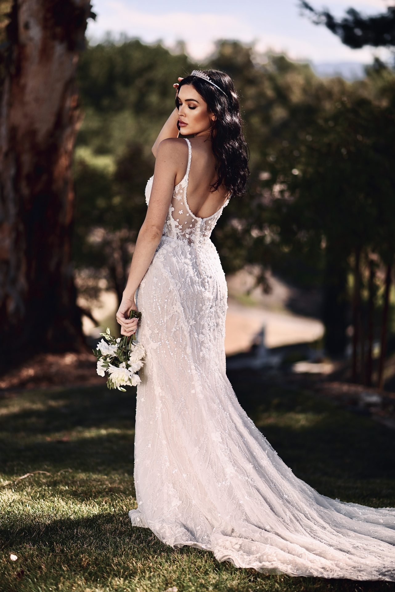 A woman in a wedding dress holding a bouquet of white flowers outdoors.