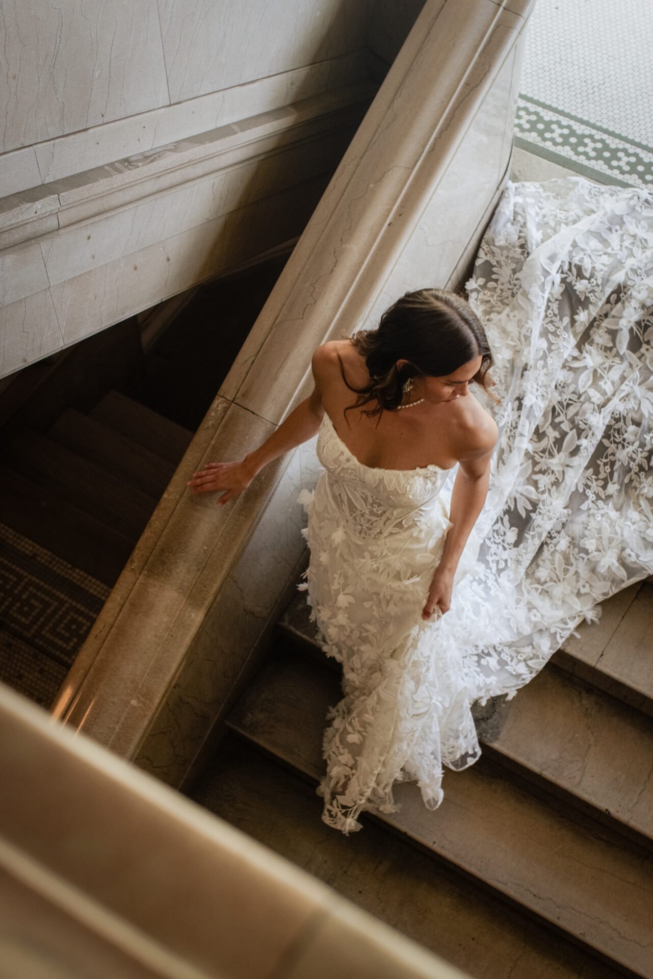 A woman in an elegant white wedding dress descending a marble staircase