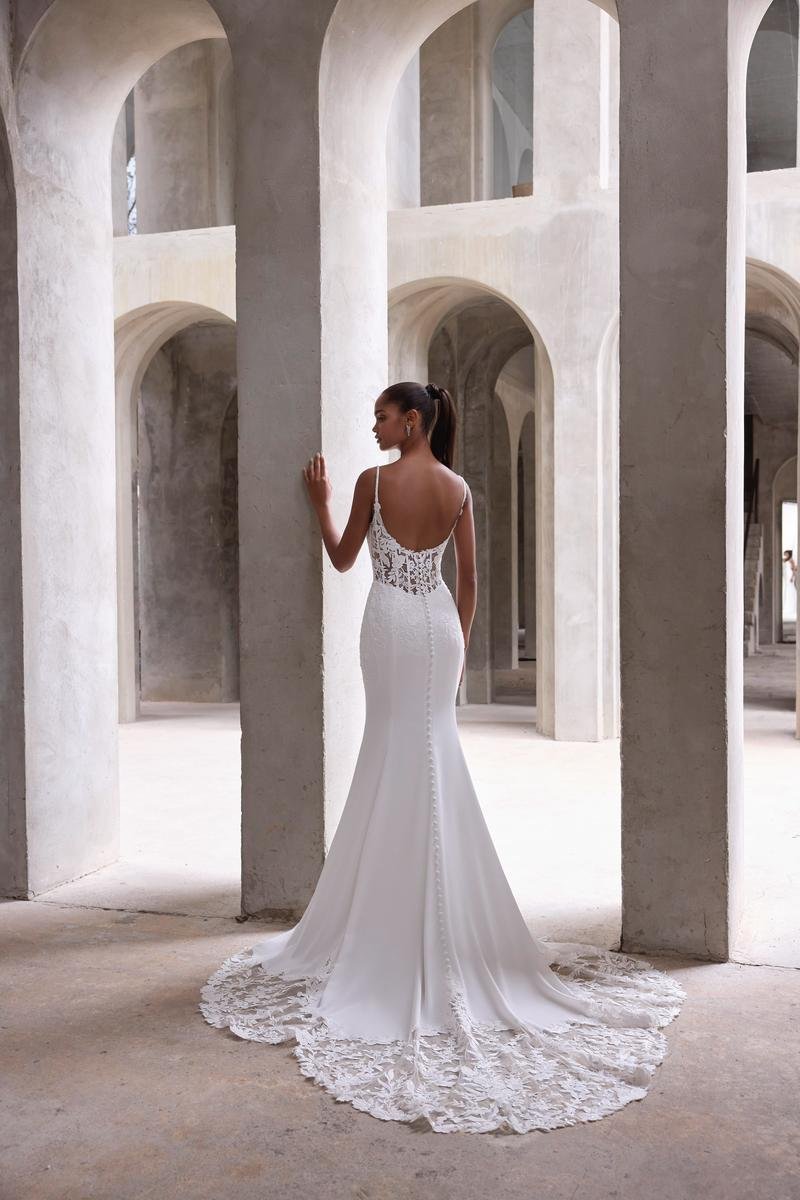 Woman in a white lace wedding dress standing in a modern architectural space with large concrete arches.