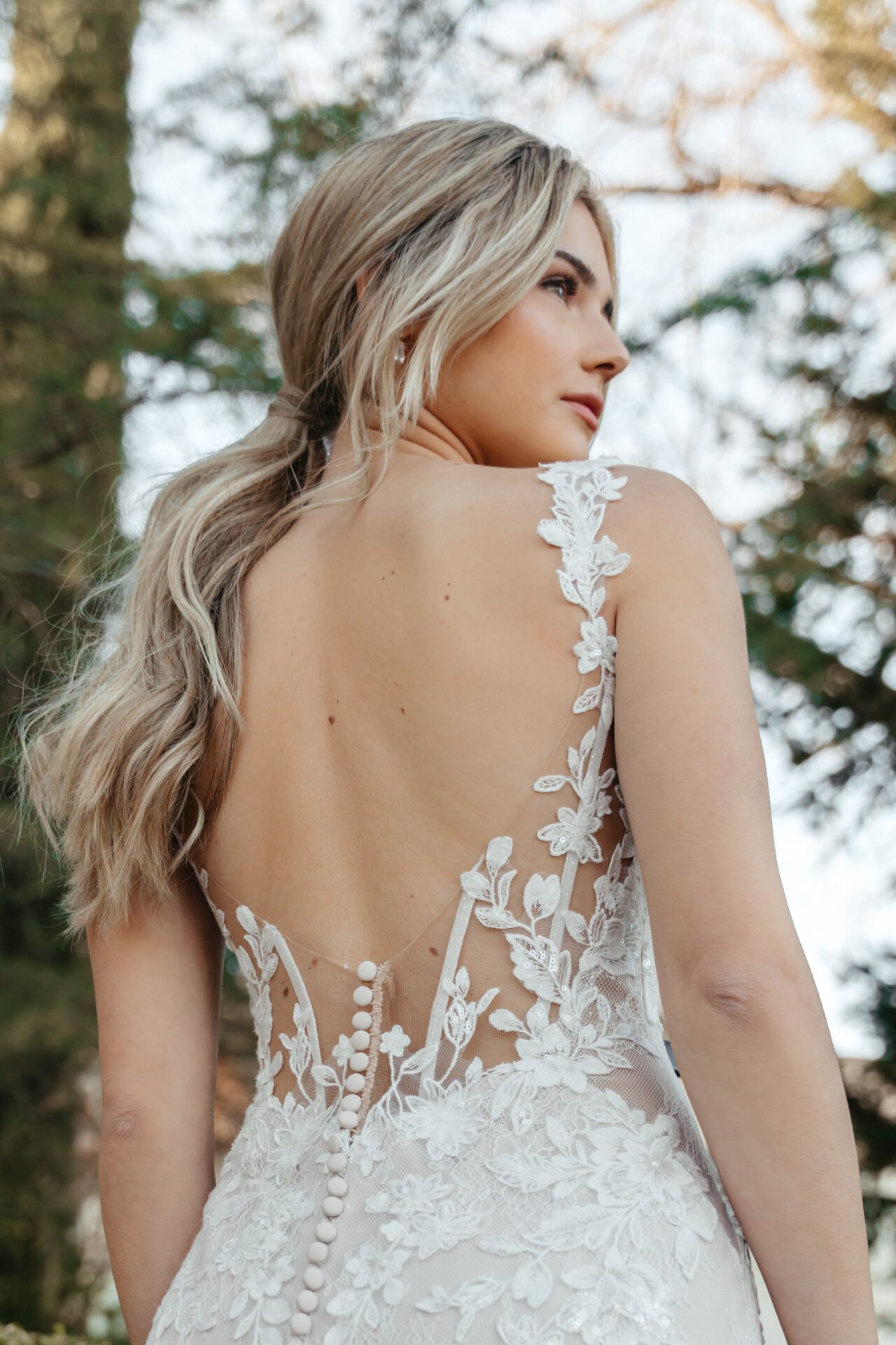 A woman in a wedding dress standing outdoors with trees in the background.