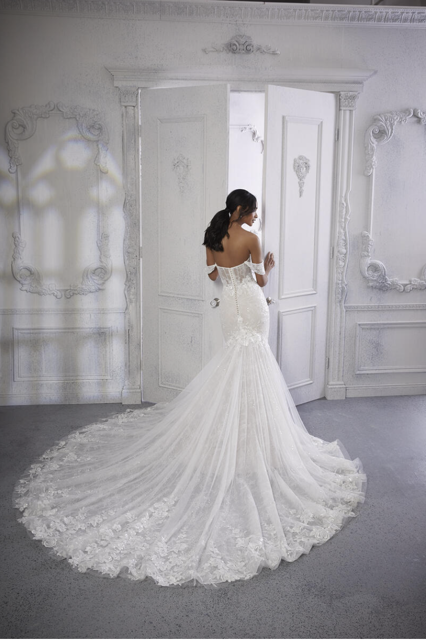 A woman in a white wedding dress standing near an open door in a decorated white room.