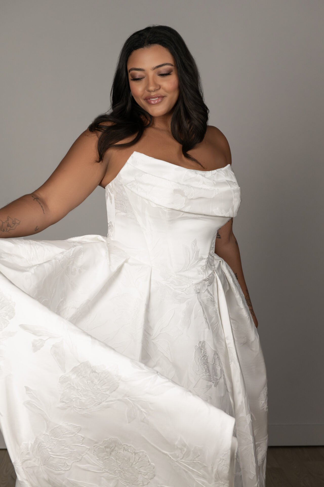 Woman in a white wedding dress smiling and looking down, holding out the fabric of her dress.