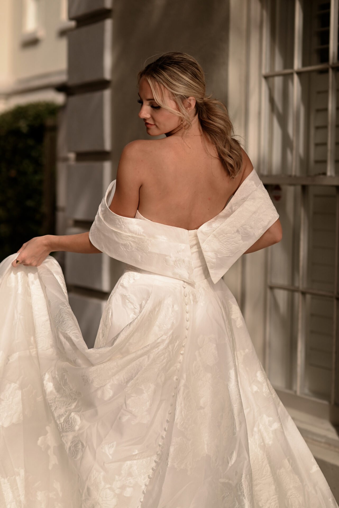 Woman in a white wedding gown, holding the skirt, standing outdoors at night.