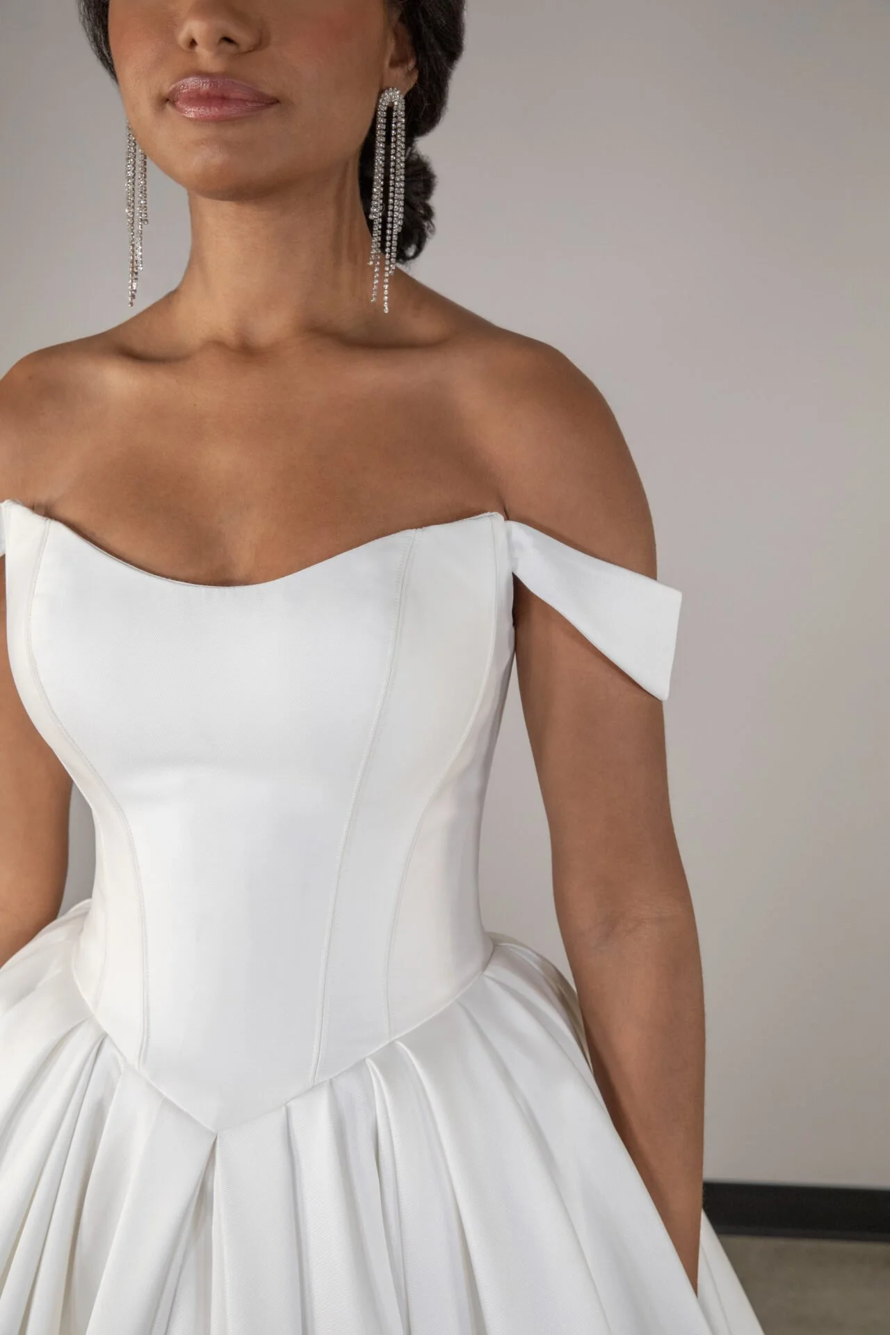 Woman wearing a white off-the-shoulder dress with pleated skirt and long, dangling diamond earrings.