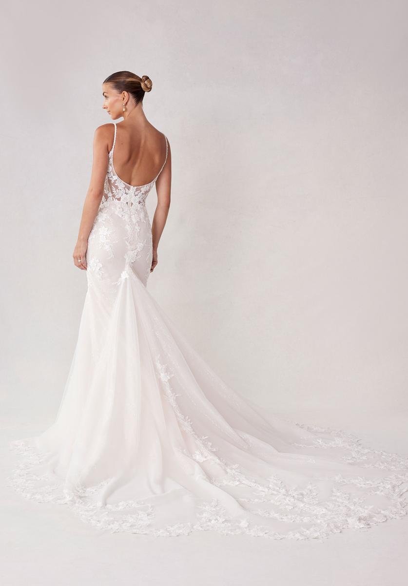 Woman wearing a white wedding dress with lace details, standing with her back to the camera against a plain light background.