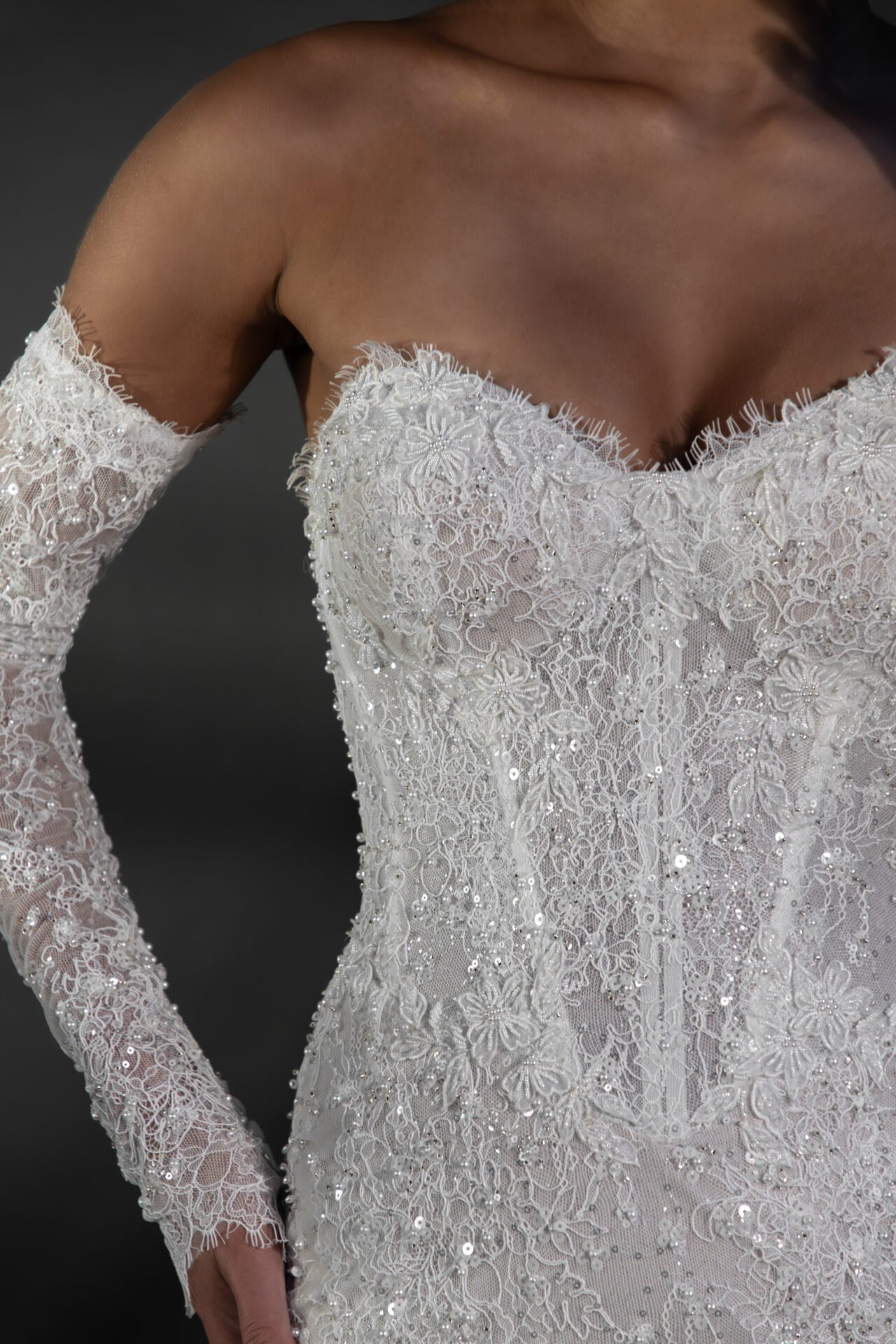Close-up of a woman wearing an off-the-shoulder white lace wedding dress with intricate floral embroidery and beadwork.