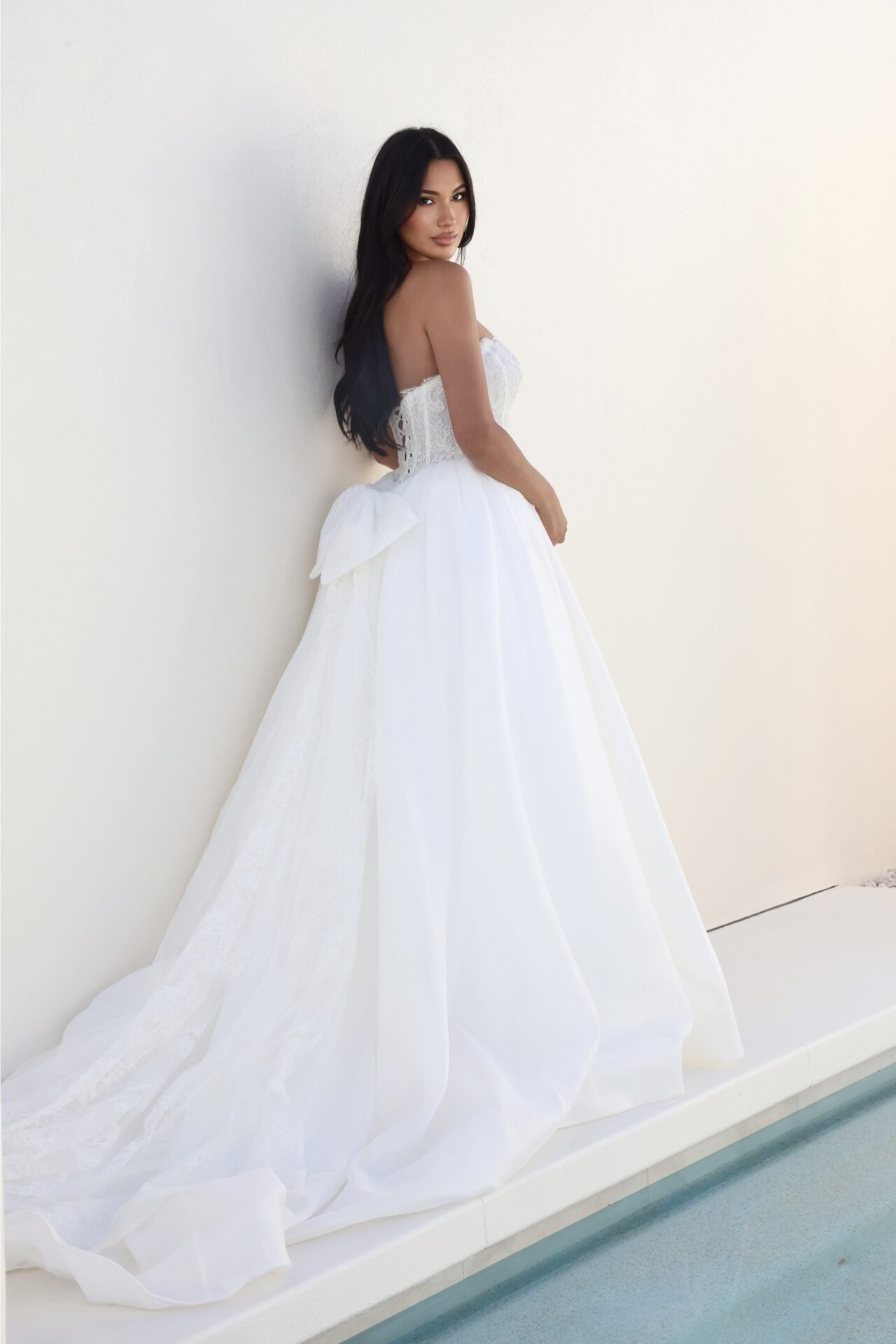 A woman in a white wedding dress standing against a plain white wall.